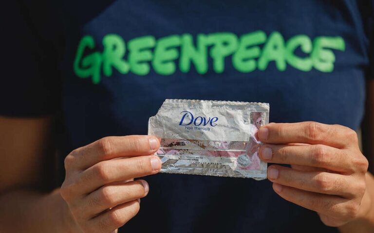 man with a greenpeache shirt holding a dove plastic sachet packaging