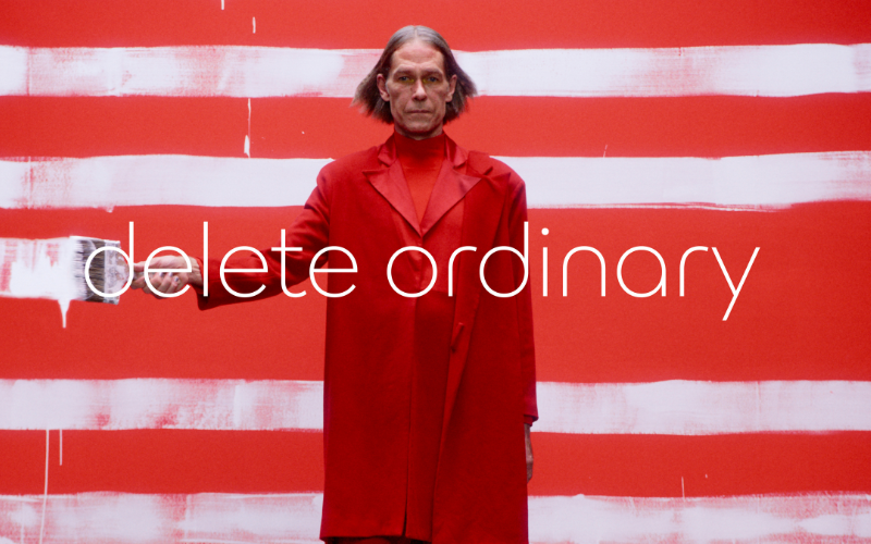 man in a red coat, standing nehind the sentence "delete ordinary"